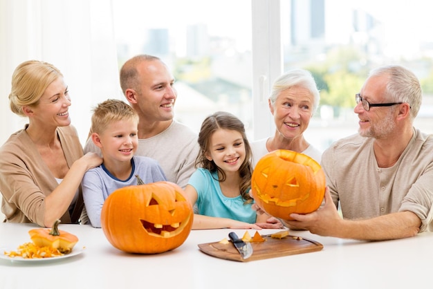 familie, glück, generation, feiertage und personenkonzept - glückliche familie, die zu hause halloween-kürbisse macht