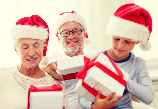 familie, glück, generation, feiertage und personenkonzept - glückliche familie in weihnachtsmannmützen mit geschenkboxen, die zu hause auf der couch sitzen