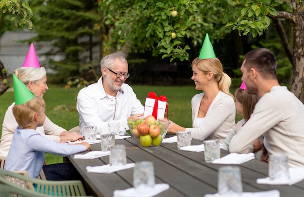 familie, glück, generation, zuhause und personenkonzept - glückliche familie mit geschenkbox beim feiertagsessen im freien
