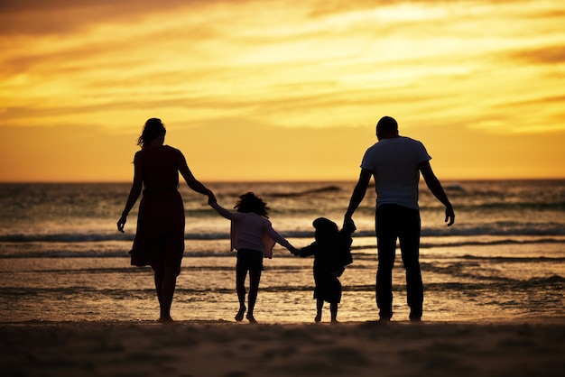 Familie Händchen haltend und Silhouette am Strand bei Sonnenuntergang Abenteuer und Liebe mit Eltern und Kindern im Freien Mutter Vater und Kinder zusammen Vertrauen und Freiheit durch die Natur und Fürsorge des Ozeans