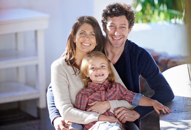 Familie im Porträt, Mutter und Vater mit Kind im Hinterhof, entspannen sich gemeinsam mit Liebe und Fürsorge im Freien. Glückliche Gesichter von Menschen außerhalb des Hauses, die sich lächelnd umarmen, und eine Frau, ein Mann und ein Mädchen in einem Garten