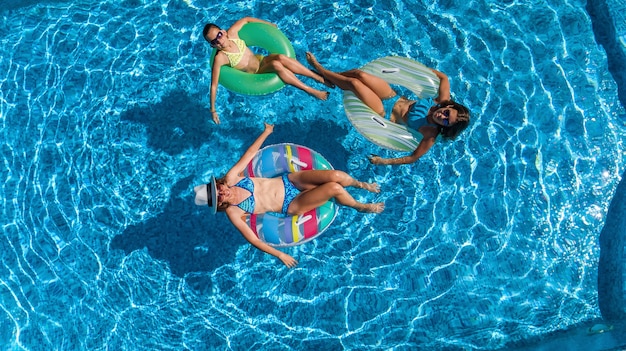 Familie im Schwimmbad Luftbild von oben, glückliche Mutter und Kinder schwimmen auf aufblasbaren Ringkrapfen und haben Spaß im Wasser im Familienurlaub, tropische Ferien im Resort