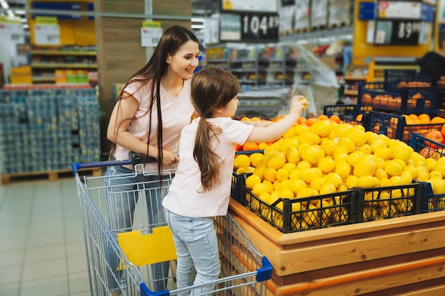 Familie im Supermarkt Junge Mutter und ihre kleine Tochter lächeln und kaufen Lebensmittel Gesundes Ernährungskonzept Mutter und Tochter kaufen Gemüse und Obst im Supermarkt