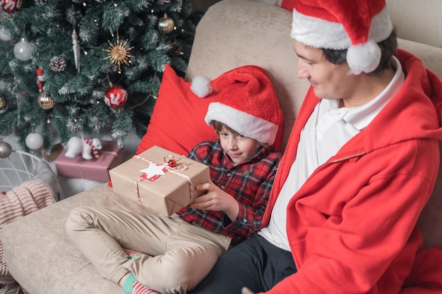 Familie in Weihnachtsmütze Vater und Kind Sohn öffnen Weihnachtsgeschenk zu Hause auf einer Couch im