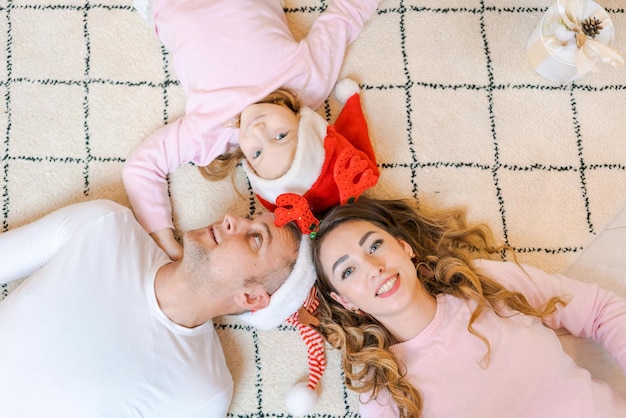 Familie in Weihnachtsmützen mit ihrer Tochter in leichter gemütlicher Kleidung liegend