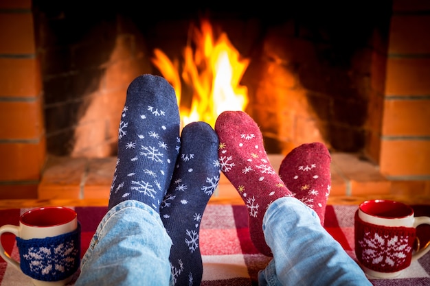 Familie in Weihnachtssocken in der Nähe von Kamin. Mutter; Vater und Baby haben Spaß zusammen. Menschen, die sich zu Hause entspannen