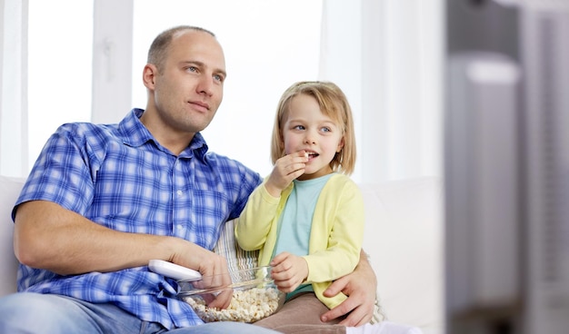 familie, kinder, elternschaft menschenkonzept - glücklicher vater und tochter, die popcorn essen und zu hause fernsehen