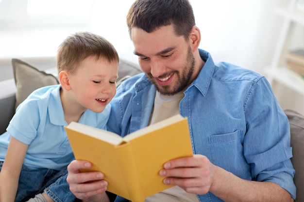 Familie, Kindheit, Vaterschaft, Freizeit und Menschenkonzept - Porträt eines glücklichen lächelnden Vaters und eines kleinen Sohnes, die zu Hause auf dem Sofa ein Buch lesen