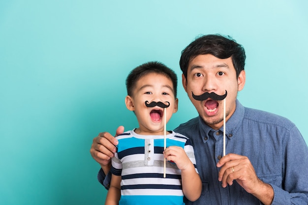 Familie lustiger glücklicher Hipster-Vater und sein Sohn halten schwarze Schnurrbart-Requisiten für Fotokabinen-nahes Gesicht