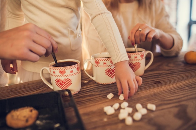 Familie Mama Papa und Tochter in weißen Pullovern kochen und trinken Kakao mit Marshmallows