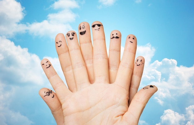 Familie, Menschen und Körperteile Konzept - Nahaufnahme von zwei Händen, die Finger mit Smiley-Gesichtern über blauem Himmel und Wolkenhintergrund zeigen