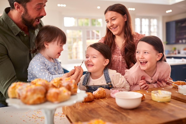 Familie mit Down-Syndrom-Tochter backt und dekoriert Kuchen, die zu Hause am Tisch sitzen