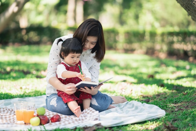 Familie mit Kindern, die Picknick im Frühlingsgarten genießen Eltern und Kinder, die Spaß beim Mittagessen im Freien im Sommerpark haben Mutter und Tochter malen im Garten