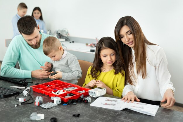 Familie mit Kindern in einem Robotikclub stellt einen Roboter her, der von einem Konstrukteur gesteuert wird.