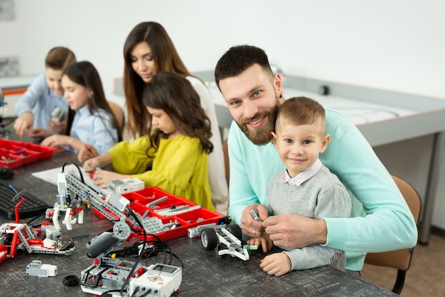 Familie mit Kindern in einem Robotikclub stellt einen Roboter her, der von einem Konstrukteur gesteuert wird.