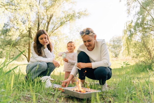 Familie mit kleinem Kind, Teenager und Großmutter beim Grillen in der Natur Einweg-Barbecue-Grill