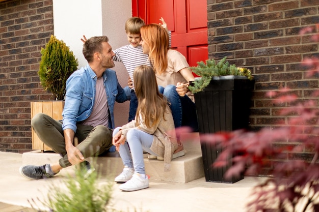 Familie mit Mutter, Vater, Sohn und Tochter, die draußen auf den Stufen der Veranda eines Backsteinhauses sitzen