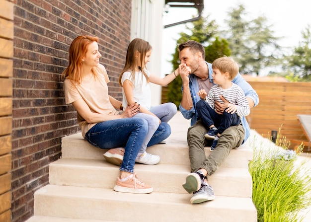 Familie mit Mutter, Vater, Sohn und Tochter, die draußen auf den Stufen der Veranda eines Backsteinhauses sitzen