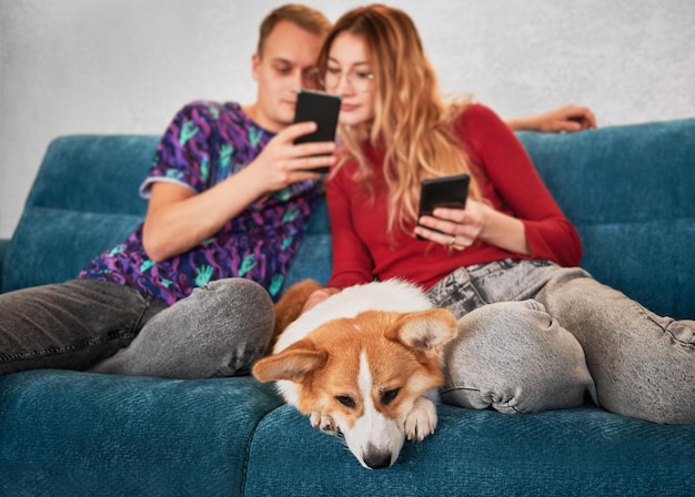 Familie mit Smartphones sitzt mit Hund auf Couch