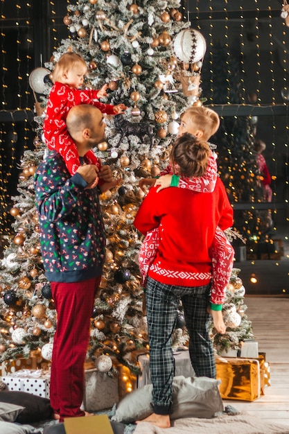 Familie mit zwei Kindern im Arm freut sich zu Weihnachten am Weihnachtsbaum