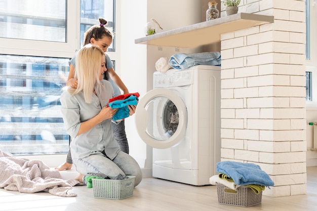 familie mutter und kind mädchen kleiner helfer in der waschküche in der nähe von waschmaschine und schmutziger kleidung