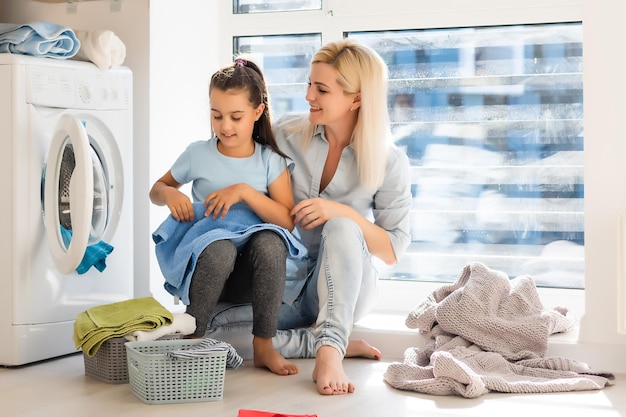 familie mutter und kind mädchen kleiner helfer in der waschküche in der nähe von waschmaschine und schmutziger kleidung