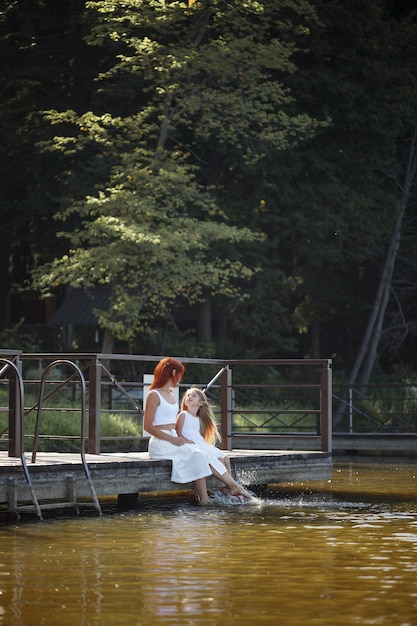 Familie, Mutter und Tochter sitzen am Fluss. Kleines Mädchen mit ihrer Mutter. Mädchen in weißen Kleidern. Familienzeit zusammen.