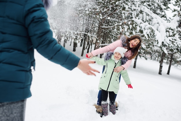 Familie, Mutter und zwei Töchter haben Spaß und spielen vor dem Hintergrund schneebedeckter Bäume und Wälder. Winterspaß