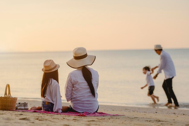 Familie, Reisen, Strand, Entspannung, Lifestyle, Urlaubskonzept. Eltern und Kinder, die im Urlaub bei Sonnenuntergang ein Picknick am Strand genießen.