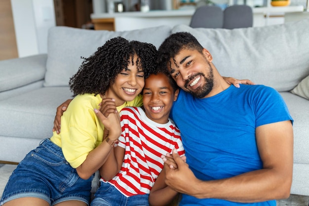 Familie sitzt auf dem Sofa und lächelt in die Kamera auf modernem Apartmenthintergrund Glückliche Familie mit Tochter, die zu Hause und am Wochenende für die Familie spielt