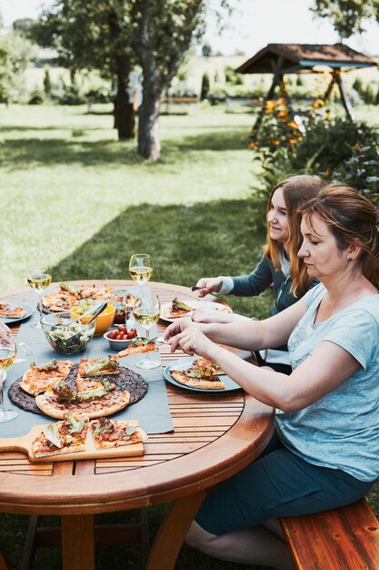 Foto familie und freunde beim essen - pizza, salate, obst und weißwein beim sommerpicknick