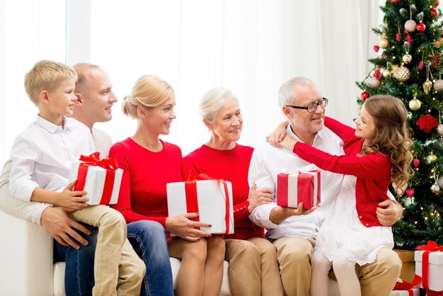 familie, urlaub, generation, weihnachten und personenkonzept - lächelnde familie mit geschenkboxen, die zu hause auf der couch sitzen