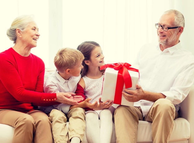 familie, urlaub, generation, weihnachten und personenkonzept - lächelnde großeltern und enkelkinder mit geschenkbox, die zu hause auf der couch sitzen