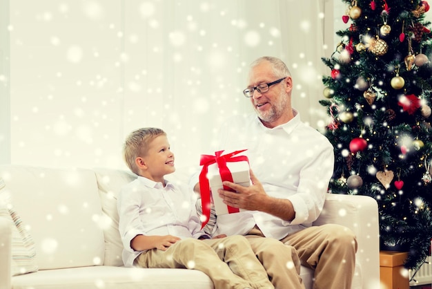 familie, urlaub, generation, weihnachten und personenkonzept - lächelnder großvater und enkel mit geschenkbox sitzen auf der couch zu hause