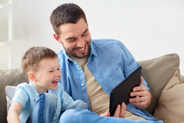 Familie, Vaterschaft, Technologie und Menschen Konzept - glücklicher Vater und kleiner Sohn mit Tablet-PC-Computer sitzen zu Hause auf dem Sofa