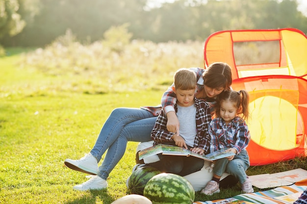 Familie verbringt Zeit zusammen. Mutter mit zwei Kindern liest Buch im Freien in Picknickdecke und Kinderzelt.