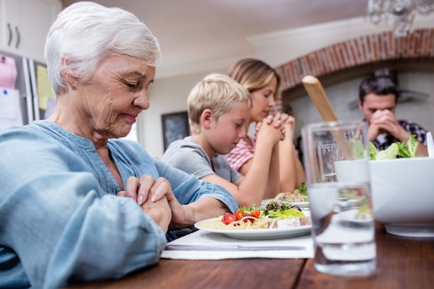 Familie von mehreren Generationen, die bevor Mahlzeit betet