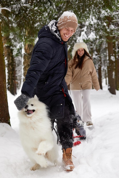 Familie von Mutter, Vater und Sohn, die sich im verschneiten Winterholz mit fröhlichem Schoßhund amüsieren