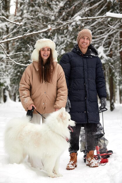 Familie von Mutter, Vater und Sohn, die sich im verschneiten Winterholz mit fröhlichem Schoßhund amüsieren