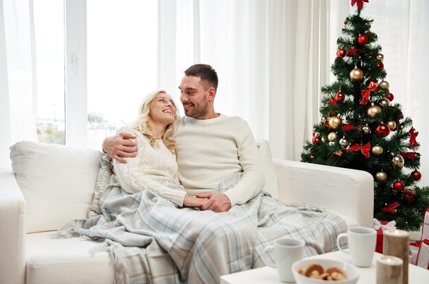 familie, weihnachten, feiertage, liebe und personenkonzept - glückliches paar bedeckt mit plaid, das zu hause auf sofa sitzt