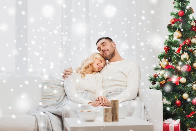 familie, weihnachten, feiertage, liebe und personenkonzept - glückliches paar bedeckt mit plaid, das zu hause auf sofa sitzt