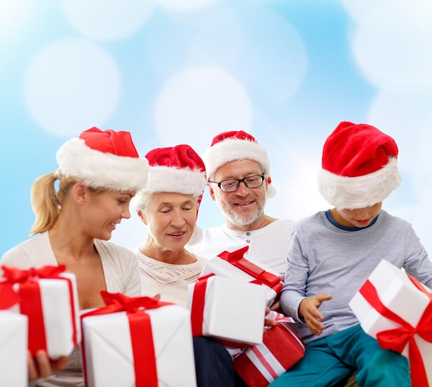 familie, weihnachten, generation, feiertage und personenkonzept - glückliche familie in weihnachtsmannmützen mit geschenkboxen, die über blauem lichthintergrund sitzen