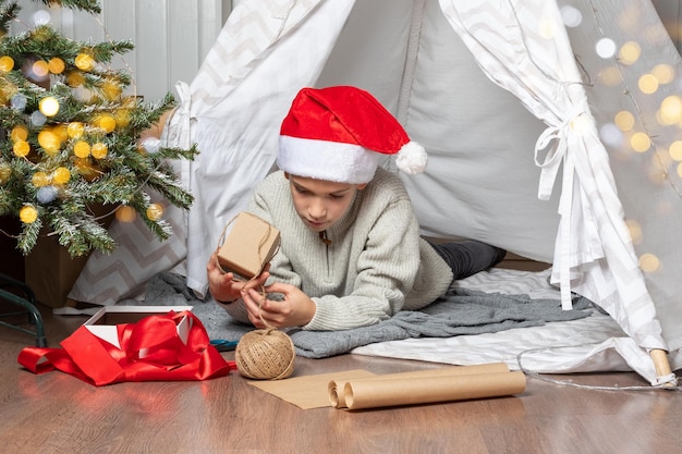 Familie Weihnachten Kinder öffnen Weihnachtsgeschenke Ein Teenager in einem Weihnachte Hut öffnet ein Geschenk und lächelt, während er auf dem Boden des Hauses sitzt