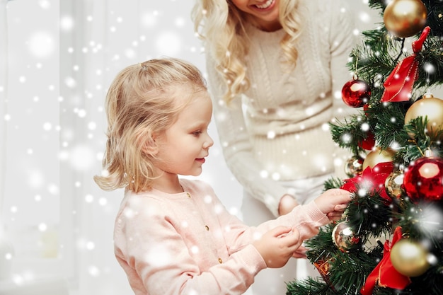 familie, weihnachten, winterferien und personenkonzept - glückliche mutter und kleine tochter, die zu hause weihnachtsbaum schmücken