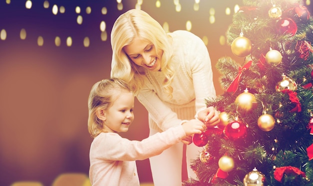 Familie, Winterferien und Menschen Konzept - glückliche Mutter und kleine Tochter schmücken Weihnachtsbaum