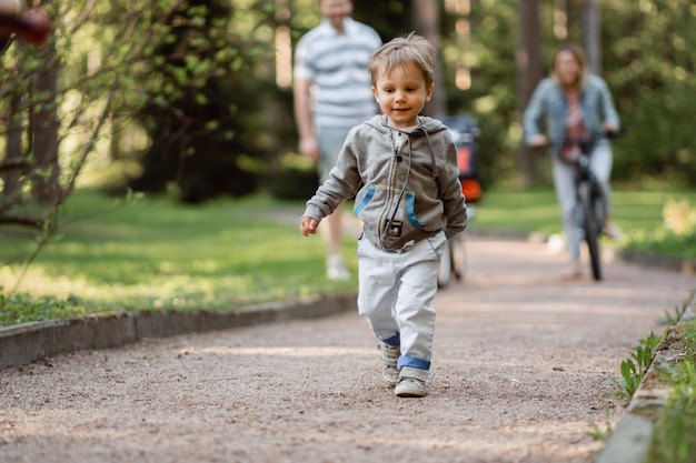 Familie zu Fuß im Park Kleiner Junge im Vordergrund Vater und Mutter Radfahren auf dem Fahrrad im Hintergrund