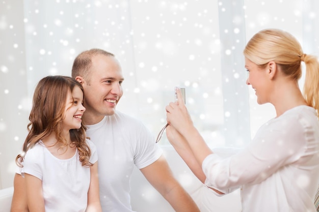 Familie, Zuhause, Technologie und Menschen - glückliche Familie mit Kamera, die ein Foto über Schneeflockenhintergrund macht