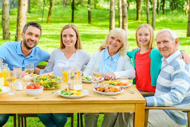 Familie zusammen. Glückliche fünfköpfige Familie, die sich miteinander verbindet und lächelt, während sie im Freien am Esstisch sitzt