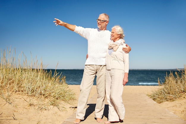 Familien-, Alters-, Reise-, Tourismus- und Personenkonzept - glückliches Seniorenpaar, das mit dem Finger auf etwas am Sommerstrand zeigt