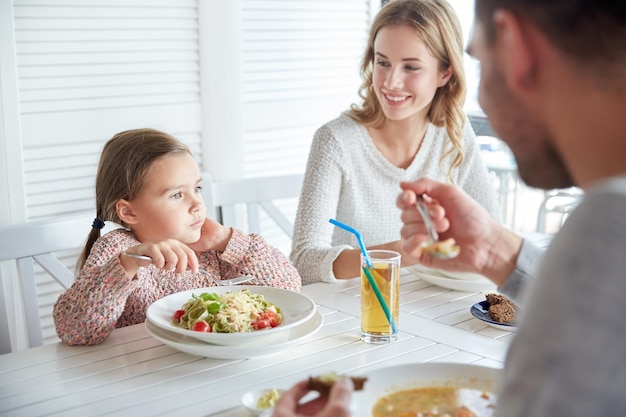 Familien-, Elternschafts-, Essens- und Personenkonzept - glückliche Mutter, Vater und kleines Mädchen essen Pasta und Suppe zum Abendessen im Restaurant oder Café